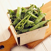 Fresh pea pods in punnet on chopping board