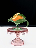 An Orange with End Sliced Off with Leaves on a Pedestal Dish