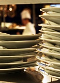 Close up of Stacked Plates in a Kitchen with Chef in Background