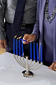 Frau zündet blaue Kerzen am Kerzenleuchter an zu Hannukah