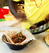 Chef Spooning Beef and Vegetable Dish onto Injera Bread in a Bowl