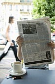 Person trinkt Kaffee und liest Zeitung in einem Strassencafe