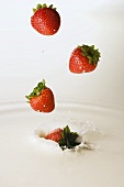 Strawberries falling into milk