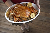 Woman Holding a Platter with a Whole Roast Chicken and Roasted Veggies