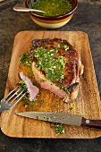Rib Eye Steak with Herb Sauce on a Cutting Board, Knife and Fork