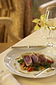 Sliced Seared Tuna on a Bed of Vegetables; On Dining Table with Wine
