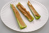 Three Celery Stalks Topped with Peanut Butter on Paper Plate