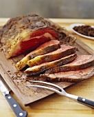 Roastbeef in Scheiben auf Holzbrett mit Fleischgabel, Messer