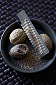 Fresh Whole and Grated Nutmeg in a Bowl with Grater