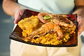 Holding Plate of Shrimp Over Yellow Rice with Tostone
