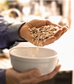 Pouring a Handful of Oats into a White Bowl