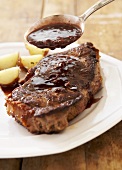 Spooning Steak Sauce Over Steak on White Plate