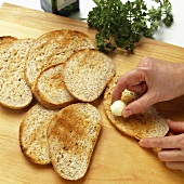 Hands Rubbing Garlic on Toasted Bread Slices