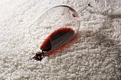 Umgekipptes Rotweinglas auf weißem Teppich