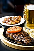 Juicy Strip Steak in a Sizzling Skillet, With Tomato and Onion, Beer