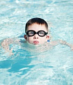 Kleiner Junge schwimmt mit Schwimmbrille im Wasser