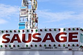 Sign for Sausage with Ferries Wheel in Background; At the Fair