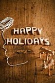 'Happy Holidays' Schriftzug aus Teig, Bindfaden und Rehfiguren auf Holzuntergrund