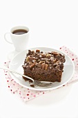 A piece of chocolate courgette cake with chocolate chips and walnut icing and a cup of coffee