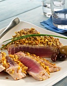 Partially Sliced Crusted Tuna on a White Plate with Olives