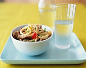 Bowl of Spicy Noodles with Pork; Glass of Water