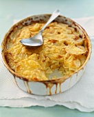 Garlic Potato Gratin in a Baking Dish with a Scoop Removed; Serving Spoon