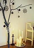A branch decorated for Christmas next to a tray of candles