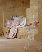 Rustikale Sitznische mit weichen Kissen und Sitzpolster; davor ein kleiner Tisch mit Wein, Obst und einer Rose