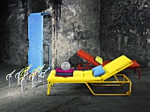 Bunte Liegestühle in Gelb, Rot und Blau vor einer verwitterten, grauen Steinfassade