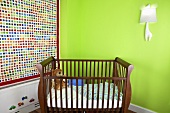 Gitterbettchen aus Holz in Kinderzimmerecke vor grüner Wand & gepunktetem Raffrollo