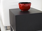 Shiny, red ceramic bowl on a square side table