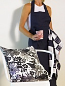 Pillow with black and white design on a chair and a woman with a black apron and cup in her hand