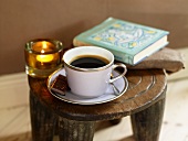 A cup of coffee, a book and a tea light on a rustic wooden stool