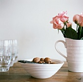 Pink roses in a jug, a bowl of walnuts and glasses