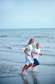 A girl and a boy running along a beach