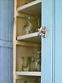 A metal door knob on a blue cupboard with an open door