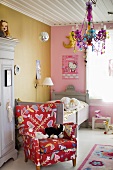 A child's room with a colourful reading chair in front of a bed and a chandelier hanging from the white wooden ceiling