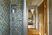 A tiled shower with taps and view through an open door into a living room