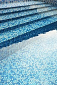 Blue mosaic tiles on stone steps leading to a pool filled with water