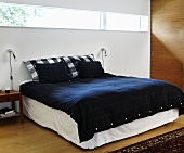 A double bed with black bedclothes and strip lighting on the wall