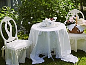 A festively laid table set with tea and a basket on a covered chair in a garden