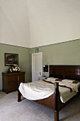 Antique wooden bed in front of a gray wall and stone floor