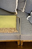 Section of a light gray sofa with a place for stowing a foot stool and a throw