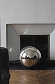 Stainless steel ball on a wood floor laid with a herringbone pattern in front of a fireplace