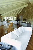 White sofa under a beam ceiling and natural stone wall in the living room of a country home