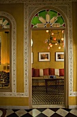 View through a rounded arch into a Moroccan living room with borders on the yellow walls and patterned tile floors