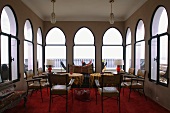 Salon mit orientalischen Spitzbogenfenstern und Lederstühlen vor Tischen auf rotem Teppich