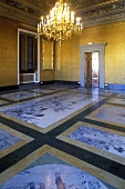 Brass chandelier in a castle's hall with painted stone floor and gold walls