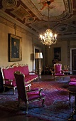 Rococo style sofa and chairs upholstered in red in the living room of a castle with a chandelier hanging from a frescoed ceiling