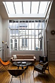 Assorted 50's style seating on a honey colored wood floor in front of an studio window and skylight